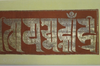 Chinese silk panel displaying the text "0m mani padme hum" (the jewel is in the lotus) in a Tibetan script with gold leaf/foil attached to a substrate of paper strips and made  ...