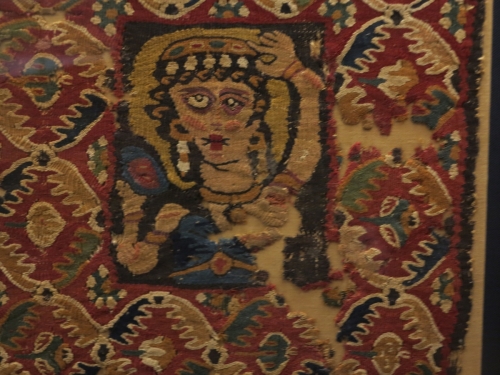 Tapestry tabula of linen and wool with the representation of a woman adorning herself in front of a mirror. These decorative textiles were sewn onto garments. 5th-6th c. 0.37x0.37 m. (ΓΕ 7111) Benaki Museum