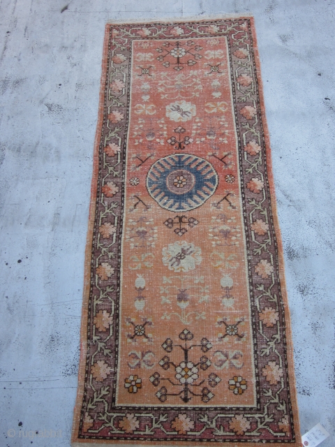 Small Khotan Runner circa 1920's , 6.8 x 2.5
A round,mid blue medallion centers a salmon field ornamented with fruits,stylized flowers,rosettes and leafy quatrefoils.The mauve-brown border of rosettes and stiff vines is also  ...