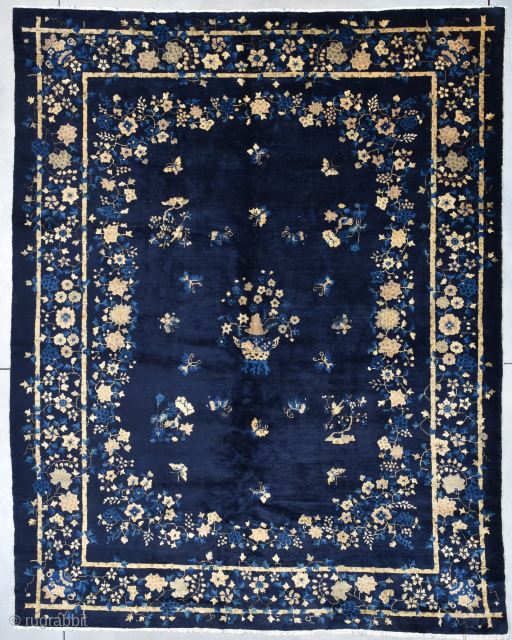 This circa 1900 Peking Chinese Oriental rug measures 9’2” X 11’7”. It has a deep indigo background. The motif has a planted pot of flowers on a four legged stool completely surrounded  ...