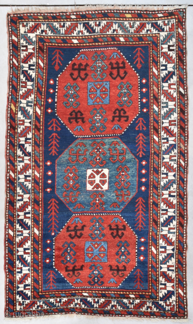 This circa 1880 Kazak Oriental Rug measures 4’7” X 7’8” (143 x 237cm). It has a dark blue ground with three eight sided medallions. The ones on the end are tomato red  ...