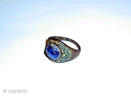 A SAPPHIRE INSET BRONZE RING PROBABLY SAMANID/ SELJUK 12TH CENTURY

The conical bezel set with a lightly faceted cabochon blue sapphire, the shank of lozenge section narrowing at each end    