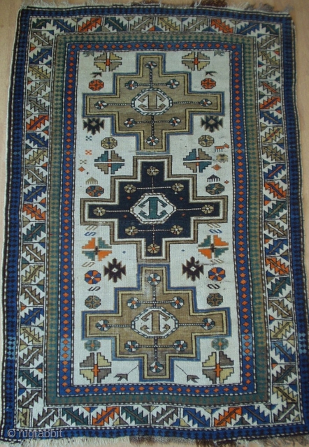 An antique Caucasian rug, (possibly Lesghi or Kazak).  Three stepped medallions in abrushed mustard & blue feature mirrored rams horns and gulls.  The unusual ivory colored background shows similar scattered  ...