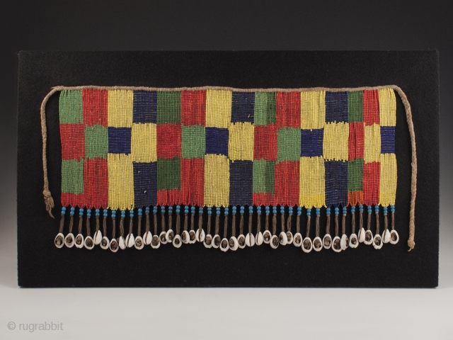 Pikuran (cache-sexe, Bana Guili people, Mandara Mountains, Cameroon. Seed beads, cotton string, cowrie shells. 16.25" (41.2 cm) wide by 8.25" (21 cm) high. With base 20.75" (52.7 cm) wide by 12.25" (31  ...