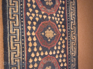 Tibetan khaden, with traditional 3 coin (?gul) design and endless knots, in blue, off white and purple,c.1900, 29 by 71 inches, some reweaving at ends.        
