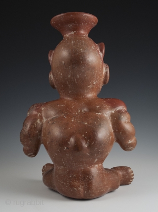 Seated dwarf vessel, Colima, West Mexico. Earthenware, slip, 11" (28 cm) high. 100 BC - 250 AD.

A reddish-brown painted earthenware seated dwarf with out-turned legs and bulging muscular arms. He wears a  ...